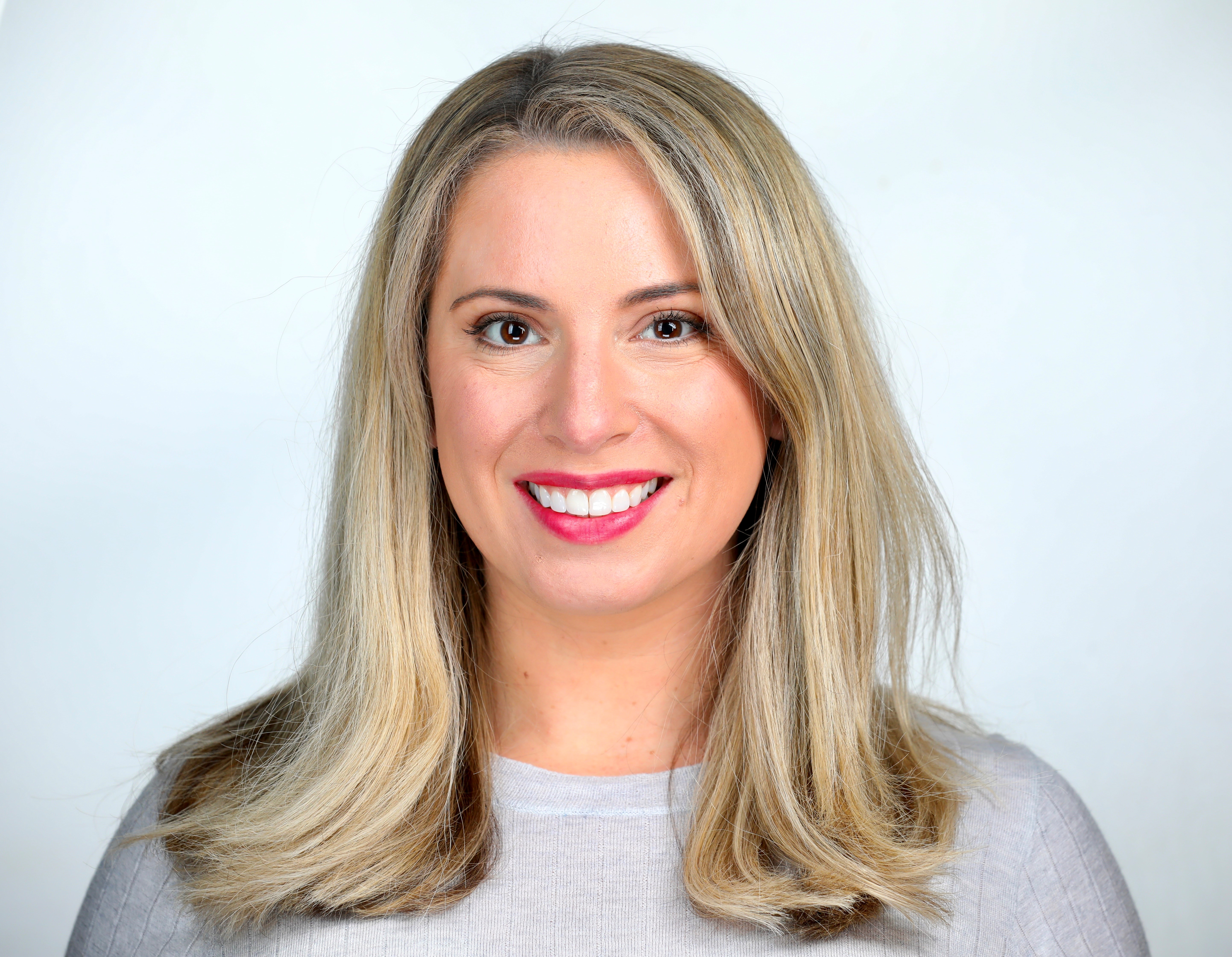 Ashley Warren: A woman with blonde hair, smiling, with pink lipstick, and a white top.