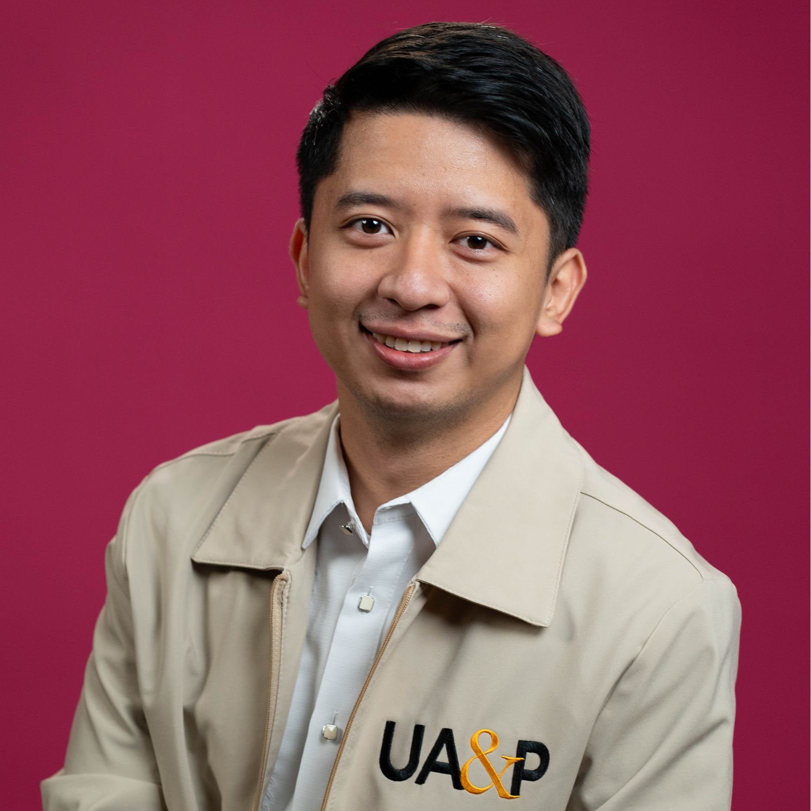 A headshot image of a man wearing a white shirt and jacket smiles warmly