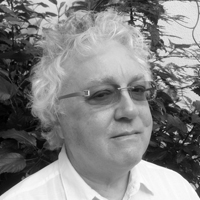A black and white headshot photograph featuring a man wearing glasses