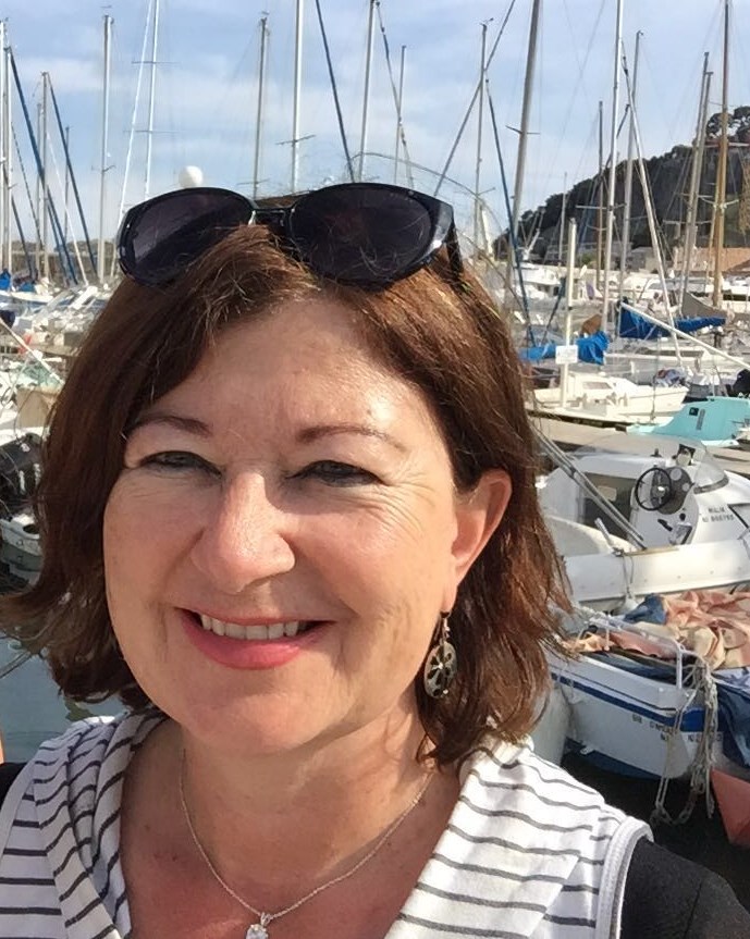 image of Liz Quick, a smiling older woman with coppery brown hair with many sailboats in the background