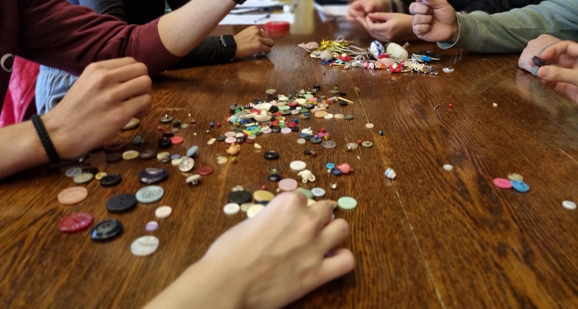 Several hands from different people around a table with piles of buttons in the middle.